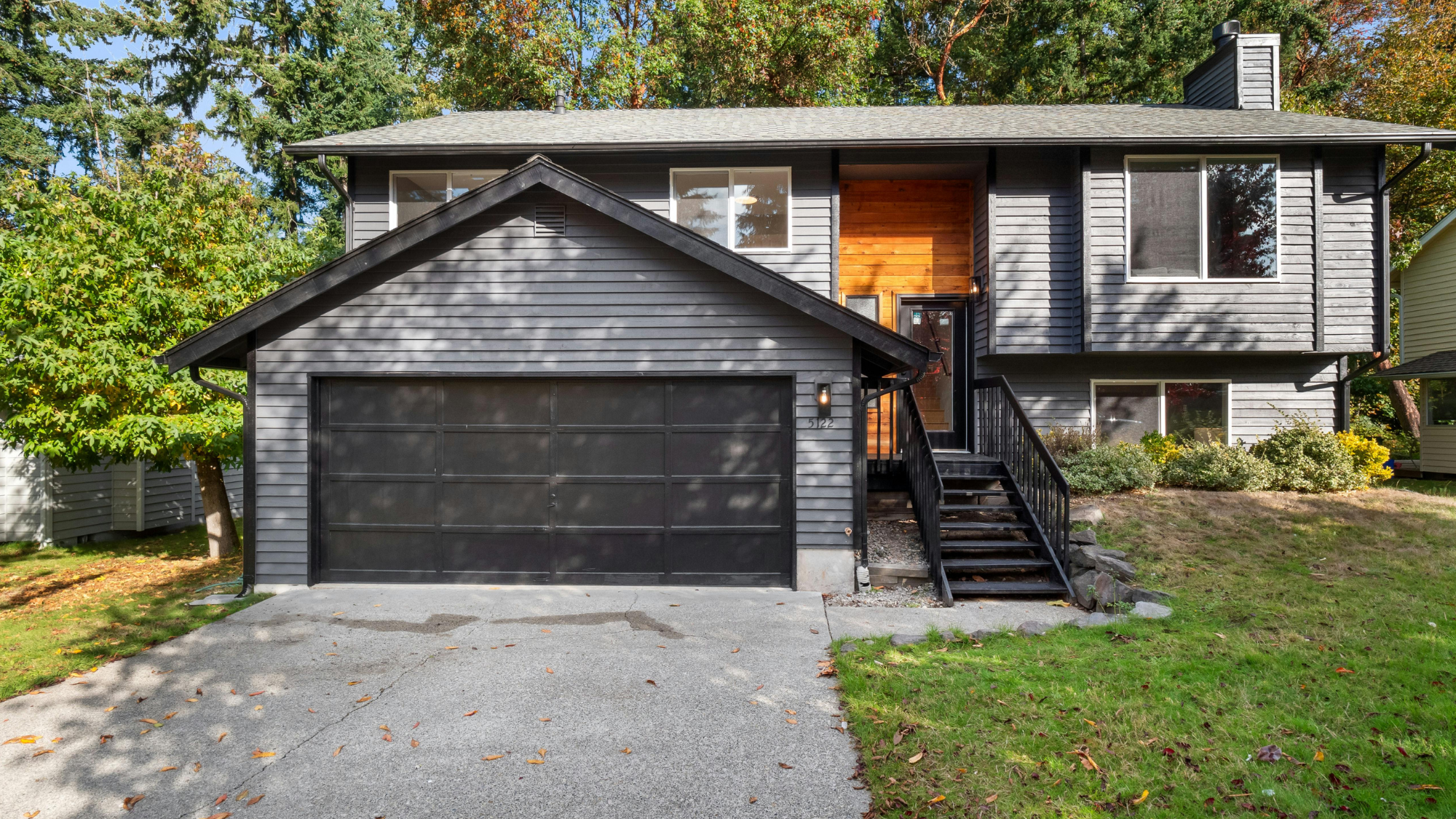 Renovated split-level house exterior with updated gray siding, a cedar entry accent and a black garage door